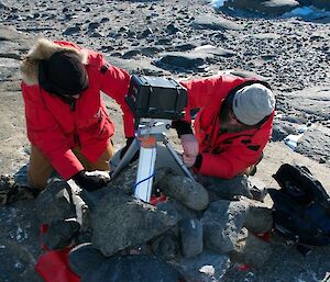 Two expeditioners reattach the solar panel bungy cord to the tripod of the nest camera