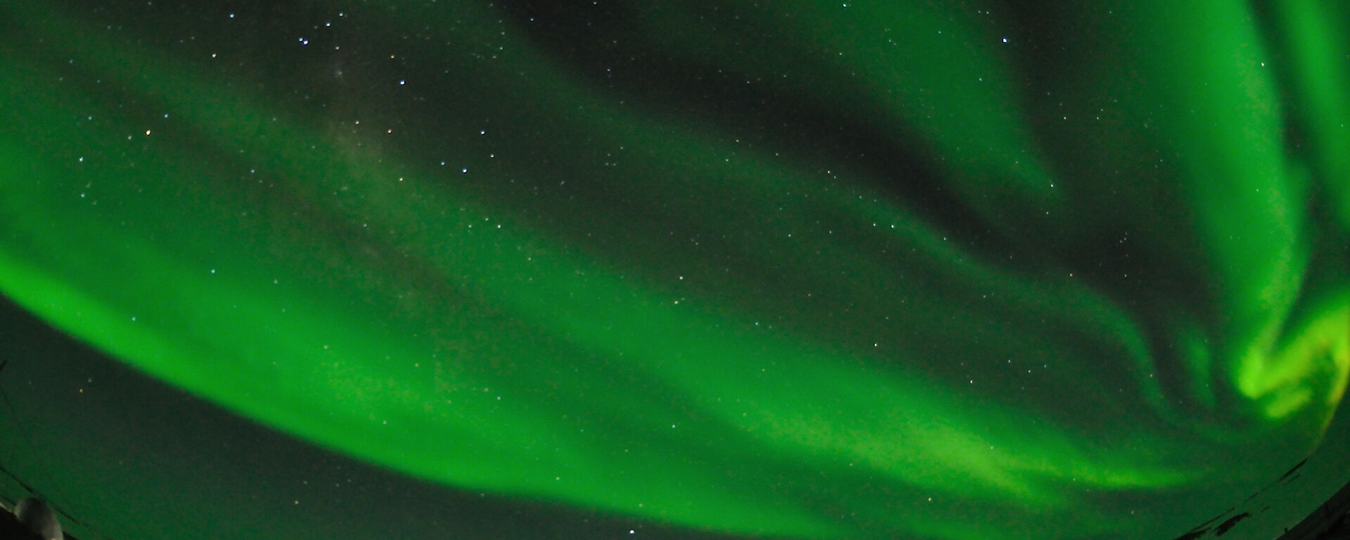 Green curtains of light fill the sky whilst the red Sleeping and Medical Quarters and a wind turbine can be seen below