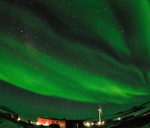 Green curtains of light fill the sky whilst the red Sleeping and Medical Quarters and a wind turbine can be seen below