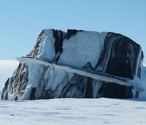 An interestingly shaped iceberg sloping slightly to one side and containing various bands of dark colour due to teh presence of moraine in the ice