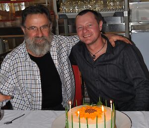 The two men celebrating their birthday sitting at a table with birthday cake and candles