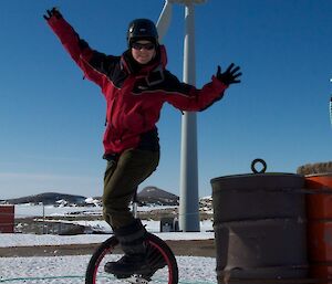 Woman on unicycle in front of wind turbine