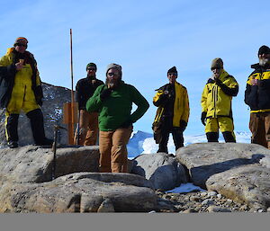 A group of six expeditioners surrounding Mawson’s Proclamation Plaque with ice creams in their hands