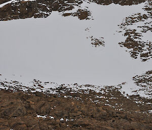 An expeditioner standing on frozen Barkell lake with the snow slopes on Chapman ridge rising behind him. Note the overhanging snow (cornice) at the top of the ridge