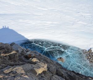 Looking down on a small lake with a cracked ice surface with a reflection of 3 people on the top of the ridge south of the ASPA