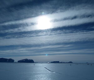 Glistening sea ice, icebergs and a cloudy sky with the sun shining through creating an unusual mood to the scene