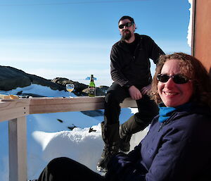 Two expeditoners relaxing on the verandah at Macey hut with a bottle of beer a cheese platter on the railing