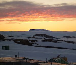 A view over the old station buildings, the ice plateau and the Casey Range and a red, orange and grey sky