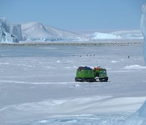 The Auster emperor penguin colony on sea ice surrounded by gigantic icebergs with the ice plateau in the background and a green Hägglunds all terrain vehicle in the foreground