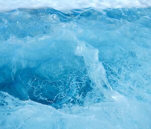 A froen lake with a scalloped surface and beautiful patterns and colours resulting from melting