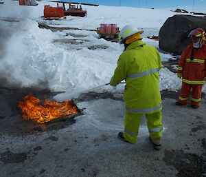An expeditioner using a dry chemical extinguisher to put out a simulated fuel fire and watched by the Fire Chief