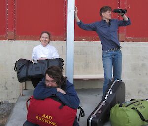 Three expeditioners with their survival gear waiting for the plane and one looking through binoculars as if looking for the plane