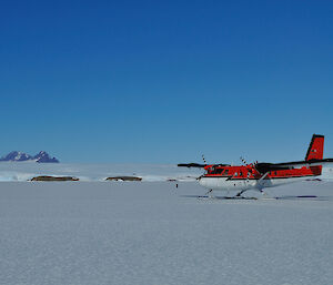 A Twin Otter landing on the sea ice with the Antarctic ice cap and mountains in the background