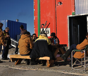 Several expeditoners sitting at a table and 3 standing relaxing with a drink and celebrating the start of summer