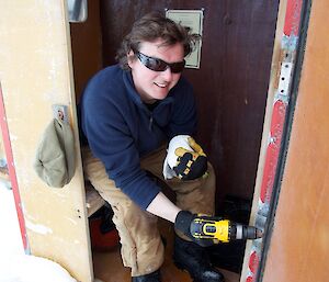 A carpenter drilling some hinges into a toilet door in a field hut