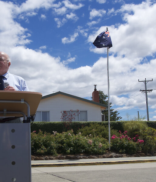 Bob Dingle’s friend and polar historian, Herbert Dartnall reads a speech at Bob’s memorial. The covered plaque on a granite boulder is behind, covered in an ANARE flag.