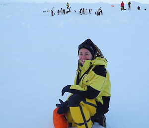 Female on sea ice with penguins behind her