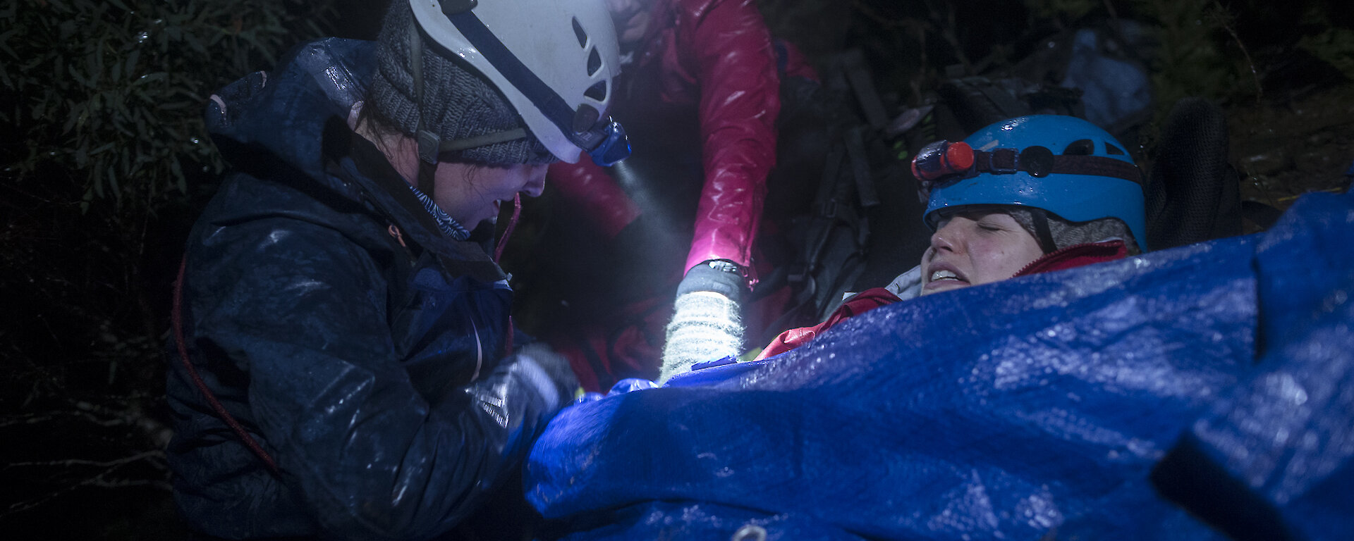 Mock patient wrapped in blanket being tended by two people.