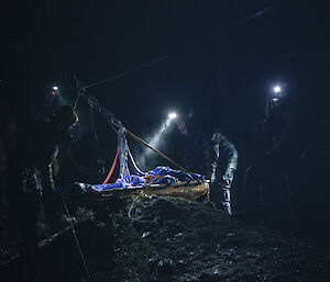 Two people carrying a stretcher in the dark with head torches.