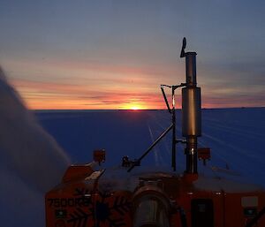 A snow blower working on the runway as the sun sets.