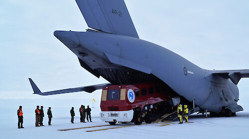 Grey cargo plane with a red bus coming out the back