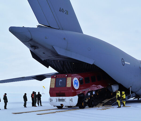 Grey cargo plane with a red bus coming out the back