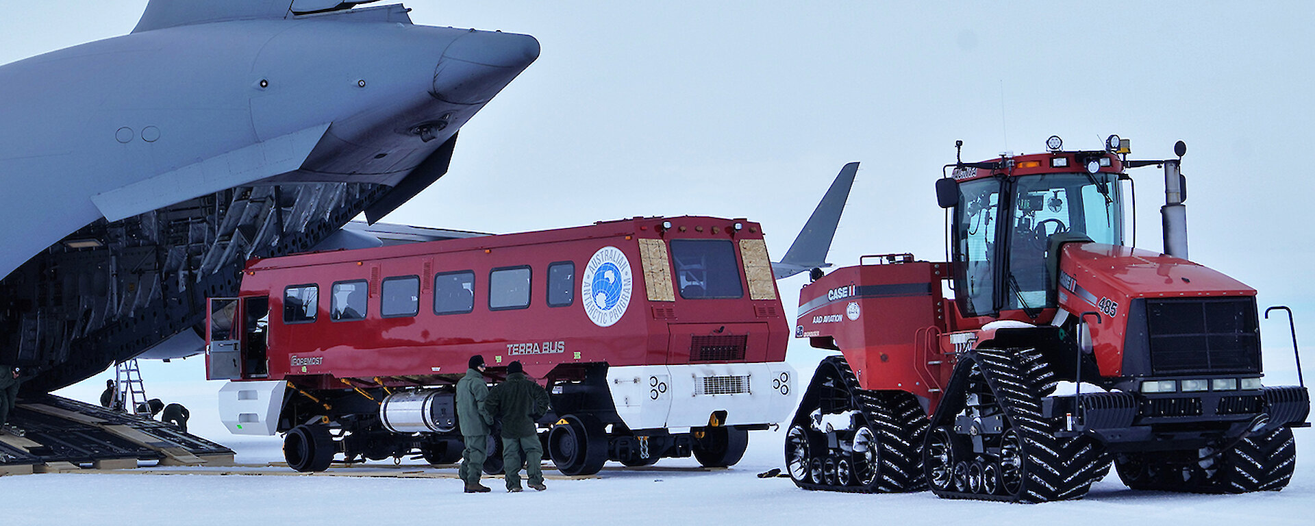 A plane with the back cargo door open and a tractor pulling out a red bus