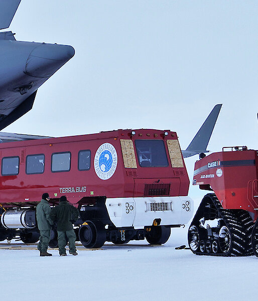 A plane with the back cargo door open and a tractor pulling out a red bus