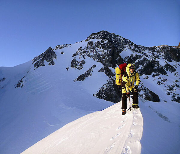 Expeditioner walking along a snow line with a mountain behind.