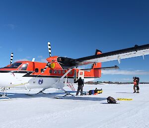 A plane on the ice with a blue sky, people loading things into it.