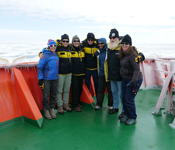 A group of 7 people standing on the deck of a ship.