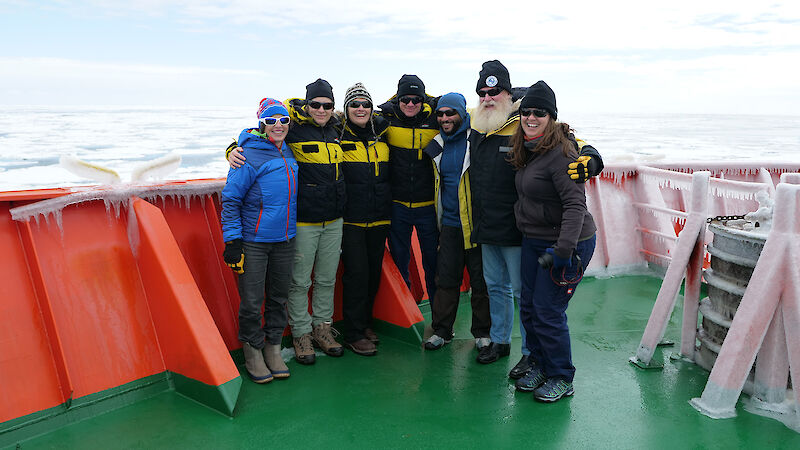 A group of 7 people standing on the deck of a ship.