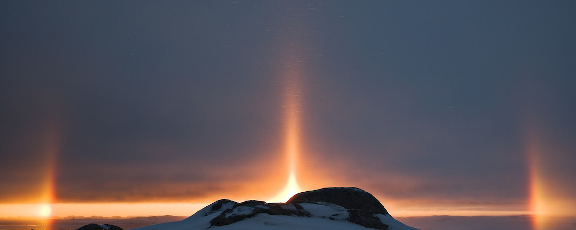 Parhelion or sun dogs on the Antarctic horizon. Sun dogs are created by light interacting with ice crystals in the atmosphere. Sun dogs typically appear as two subtly coloured patches of light to the left and right of the Sun, approximately 22° distant and at the same elevation above the horizon as the Sun.