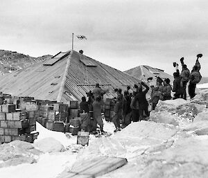 Expeditioners raise the flag after completion of the Main Hut at Commonwealth Bay in 1912.