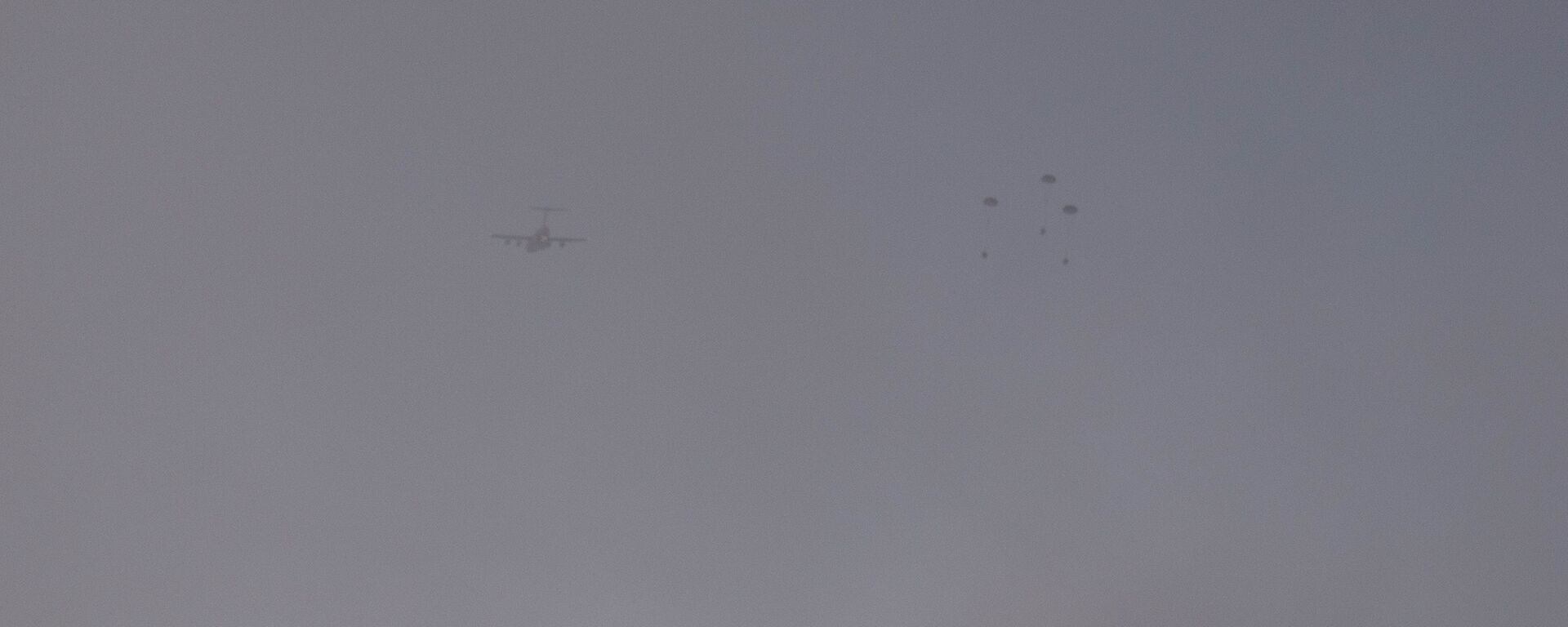 Silhouette of plane and three containers with parachutes drifting to the ground.