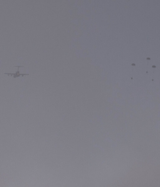 Silhouette of plane and three containers with parachutes drifting to the ground.