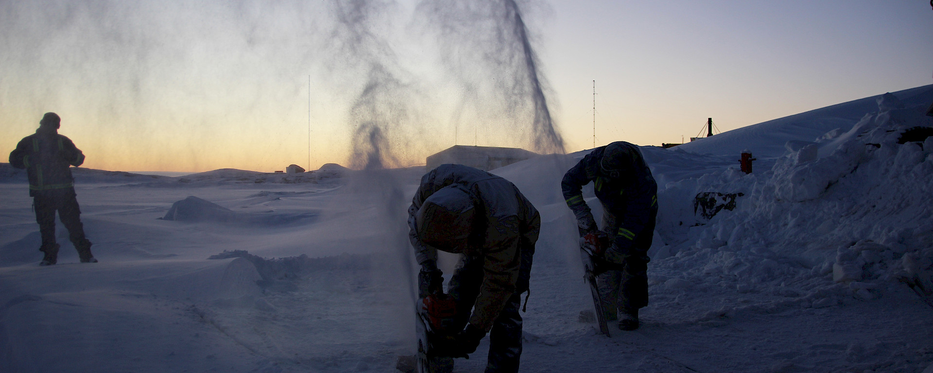 Expeditioners use a chainsaw to cut into the sea ice at Mawson station in preparation for their midwinter swim