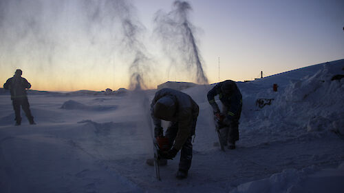 Expeditioners use a chainsaw to cut into the sea ice at Mawson station in preparation for their midwinter swim
