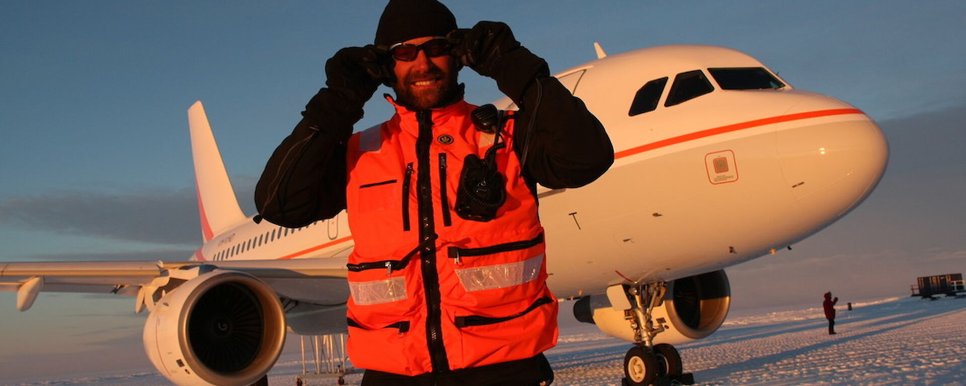 Man wearing sunglasses stands in front of aeroplane on ice.