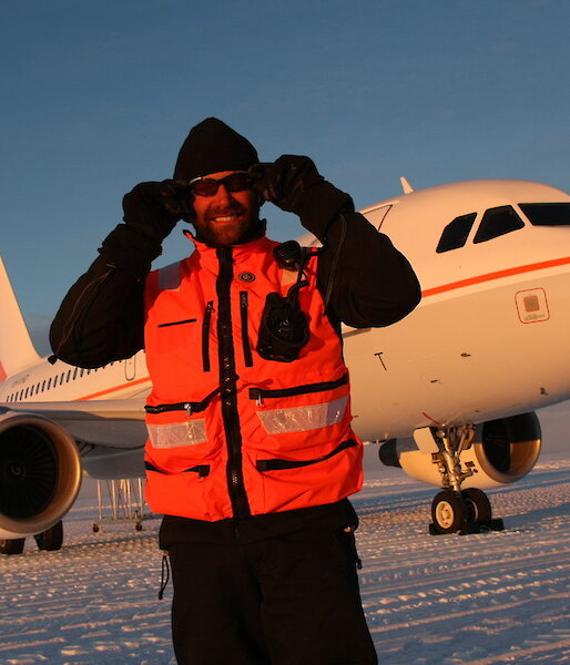 Man wearing sunglasses stands in front of aeroplane on ice.