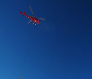 A helicopter sling loading cargo over the sea ice.