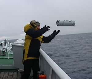 A scientist throws a small sonobuoy over the side of the ship.