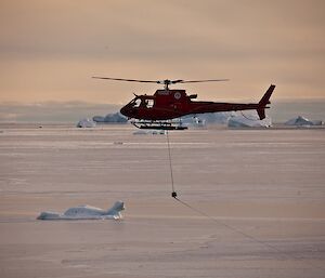 A helicopter pulls fuel lines ashore from the Aurora Australis during refuelling operations at Australia’s Davis station