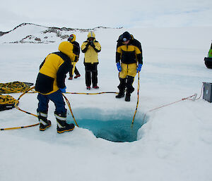 Assistants feeding out the diver’s umbilical lines as they lower the diver into the dive hole