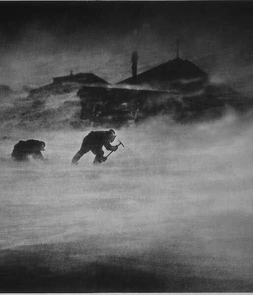 Historic image of expeditioners leaning into a ferocious wind whilst chipping ice to melt for water