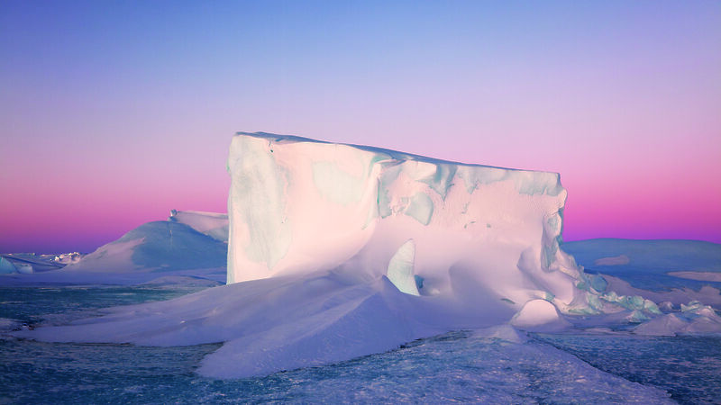 A tabular iceberg against a pink sunset.