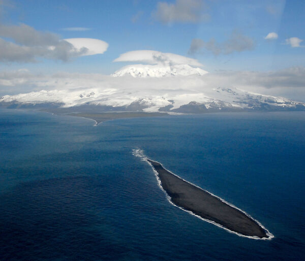 A photo from the air of a small island in the foreground and the snowy topped Big Ben on Heard Island in the background.