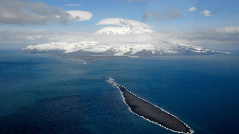 A photo from the air of a small island in the foreground and the snowy topped Big Ben on Heard Island in the background.