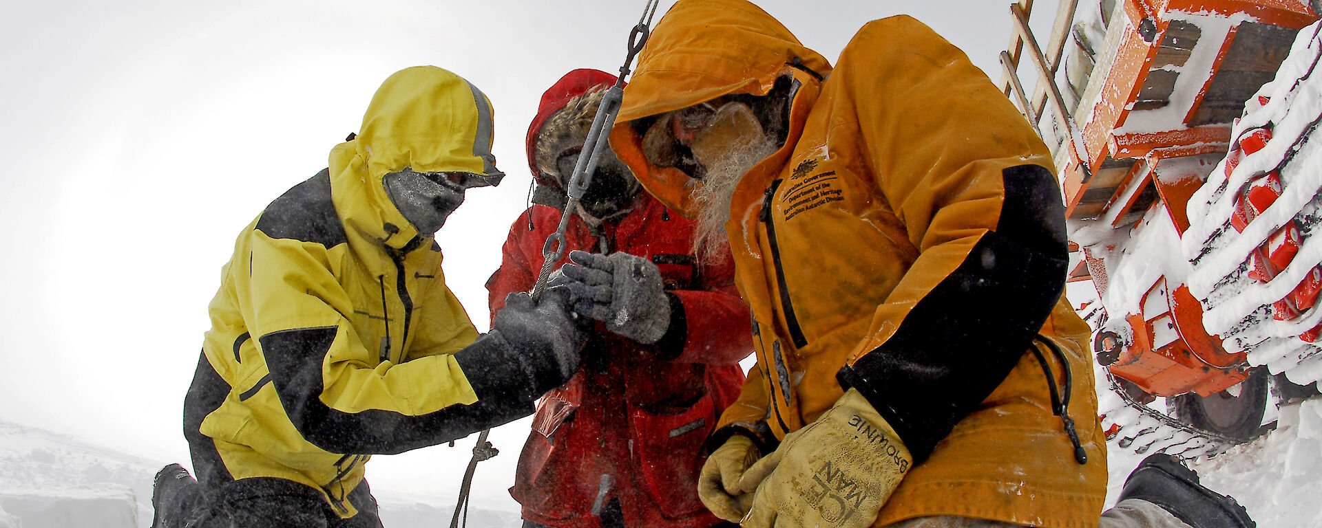 Three expeditioners outdoors gathered around a cable