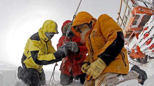 Three expeditioners outdoors gathered around a cable